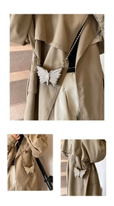 Silver butterfly crossbody bag with rhinestones and metal chain on a trench coat