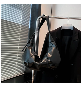 Detail of a large black glossy hobo bag with pleated texture hanging on a metal hanger