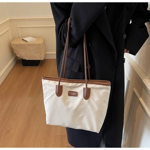 Macro detail of high-capacity tote bag featuring off-white fabric and brown leather trim