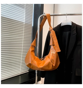 Detail of orange glossy hobo bag featuring a stylish knotted shoulder strap design