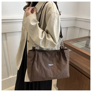 Detail of dark brown tote bag with leather tag and silver chain on beige trench coat