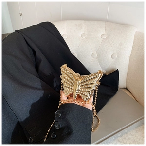 Close-up of golden butterfly chain bag with shimmering rhinestones held in hand
