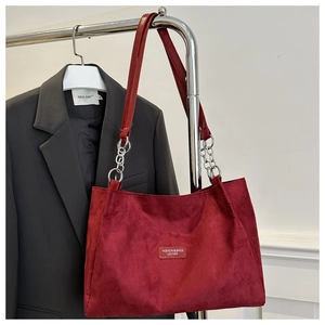 Detail of red suede tote bag with metal chain strap hanging against a grey suit jacket