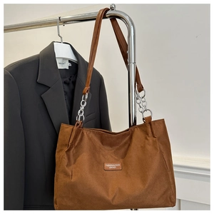 Close-up of brown tote bag with leather strap, silver chain and branded patch detail