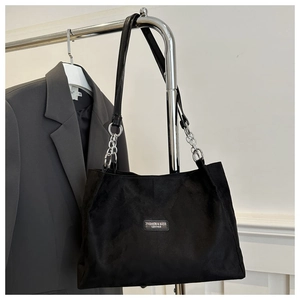 Detail of black suede tote bag featuring silver chain strap and minimalist brand label