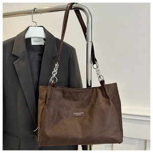 Detail of dark brown tote bag featuring leather-chain strap and embossed patch logo