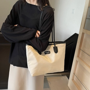 Large cream nylon tote bag with black straps worn by a model in a minimalist setting