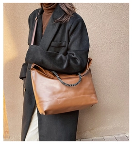 Close-up of brown leather tote bag featuring woven rope handles and adjustable strap