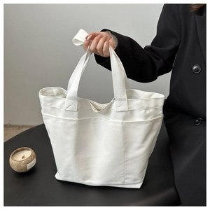 Close-up of a white canvas tote bag showing three vertical pockets and thick woven handles