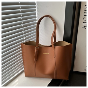Close-up of brown leather tote bag with gold lettering and adjustable straps in sunlight