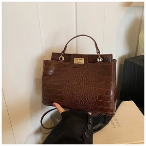 Detail of brown crocodile pattern handbag featuring a golden rectangular twist lock closure