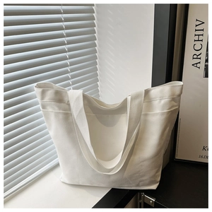 Detail view of large white canvas tote bag with functional front pocket and wide straps