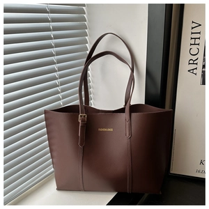Close-up of dark brown leather tote bag with gold lettering on a minimalist background