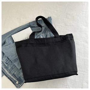 Detail of a large black canvas tote bag on textured fabric with a denim jacket