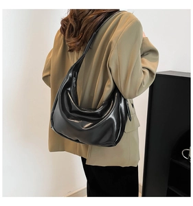 Close-up of a black leather hobo bag worn by a model in a minimalist urban setting