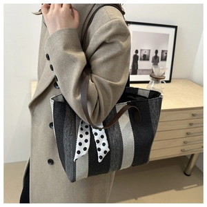 Detail of striped canvas tote bag with brown leather strap and polka dot ribbon accent