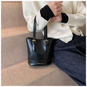 Detail of black faux leather bucket bag with gold square buckles and logo print