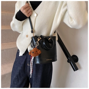 Close-up of black leather bucket bag with gold text and brown plush bear charm