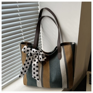 Detail of striped canvas tote bag featuring a decorative polka dot bow and leather handles