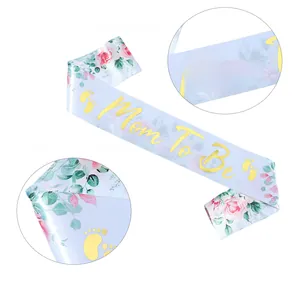 Detail of light blue Mom To Be satin sash with golden font and pink floral patterns