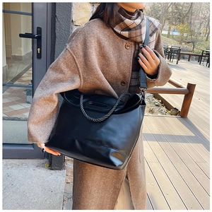 Detail of black leather tote bag featuring a woven rope handle and wide nylon shoulder strap