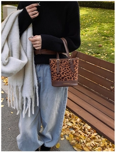 Detail of leopard print bucket bag with brown leather handle in autumn park setting