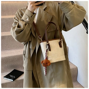 Detail of beige bucket bag with plush bear charm and printed scarf on a khaki coat