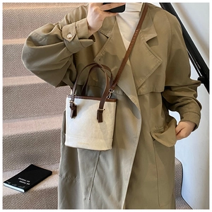 Detail of a beige and brown bucket bag showing the texture, golden hardware and shoulder strap