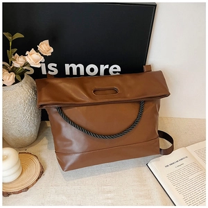 Detail of a brown leather tote with a unique fold-over handle and woven rope shoulder strap