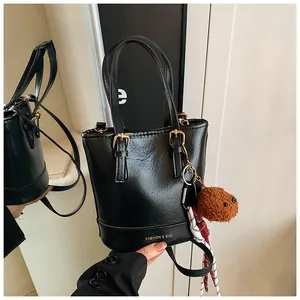 Detailed view of matte black bucket bag featuring fuzzy ball charm and brand lettering