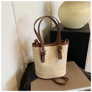 Detail of vintage bucket bag featuring beige leather and brown handle on a wooden stand