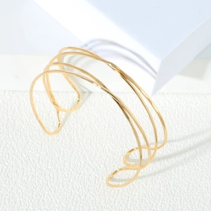 Bracelet de bras ouvert doré multicouche minimaliste sur une plateforme géométrique blanche