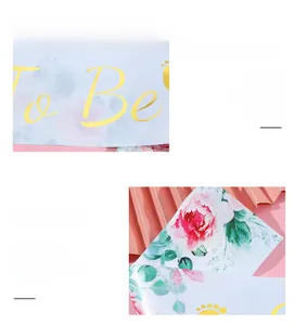 Close-up of golden foil To Be text on light blue floral satin baby shower sash