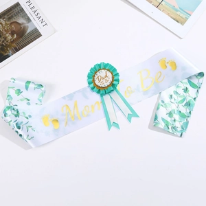 Detail of Mom to Be satin sash and Dad to Be pin with gold lettering and green foliage