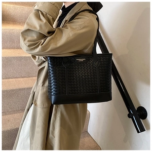 Close-up of black woven leather tote bag with a minimalist logo label and handle