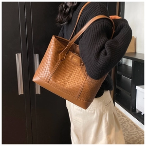 Detail of a brown woven checkerboard tote bag shown on model in a cozy indoor setting