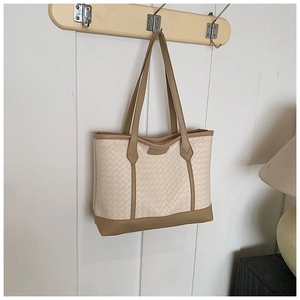 Detail of woven beige tote bag featuring brown leather trim on a wooden hanger