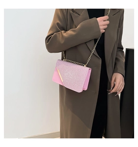 Detailed view of pink glitter crossbody bag with gold chain strap on brown coat