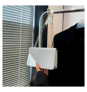 Detailed macro of silver glitter clutch bag with gold diagonal metal bar and chain strap