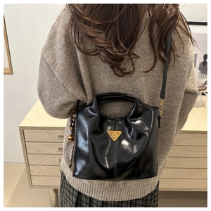 Detail of glossy black leather tote with iconic golden triangular logo and cute charms
