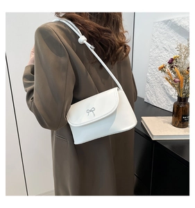 Detail of white leather crossbody bag with a metal bow accent and knotted strap on model
