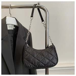 Detail of black quilted shoulder bag with chain strap against a minimalist blazer background