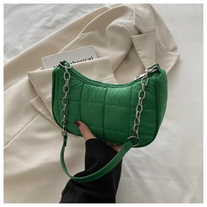 Détail du sac hobo matelassé vert avec chaîne argentée sur fond de blazer beige élégant