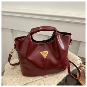Detail of burgundy glossy leather handbag with golden triangle plaque on a soft surface