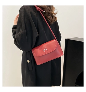 Red crossbody flap bag with silver bow accent worn over a classic black coat