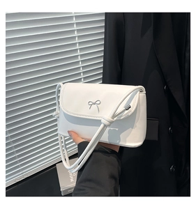 Close-up of a white leather crossbody bag featuring a decorative silver metal bow clasp
