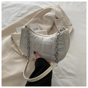Détail du sac demi-lune blanc matelassé avec chaîne argentée sur un blazer beige