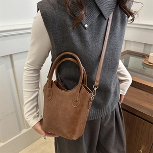 Brown minimalist bucket bag with top handle and shoulder strap in textured faux leather