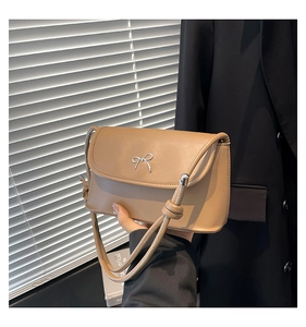 Detail of light brown crossbody bag featuring a silver metal bow and knotted shoulder strap