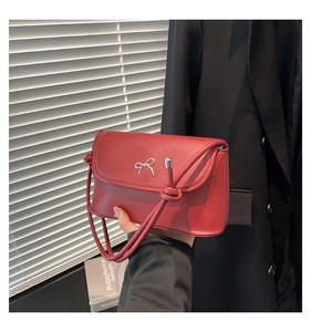 Close-up of red matte leather crossbody bag with silver bow and knotted strap detail